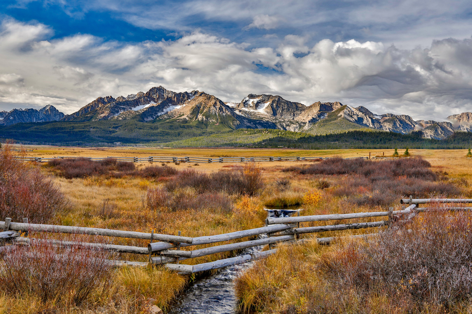 A split rail fence on the border of a large meadow with the Sawtooth mountains in the background, in the fall season near Stanley, Idaho.