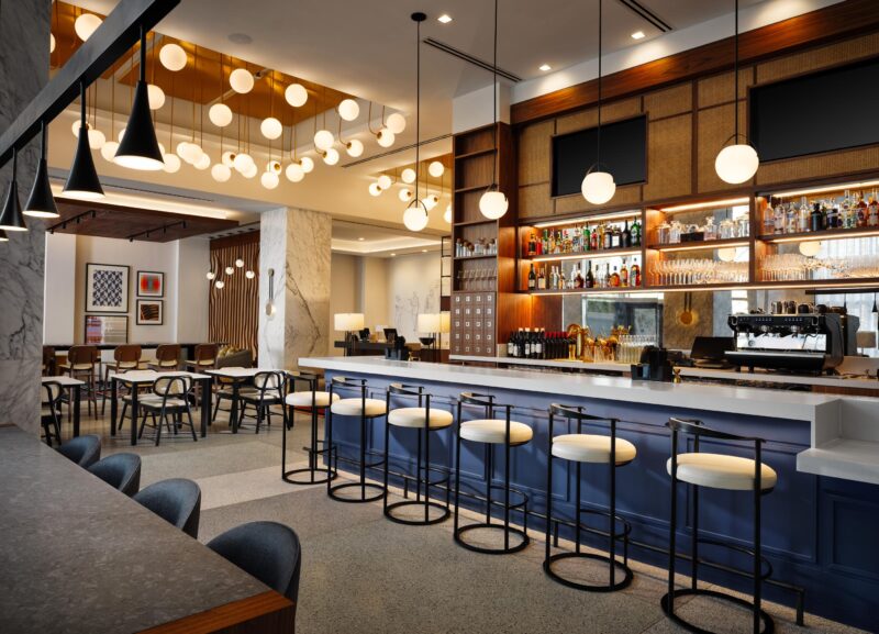 Interior bar at Hilton Canopy in New Orleans with modern lighting fixtures while warm wood features compliment a blue bar.
